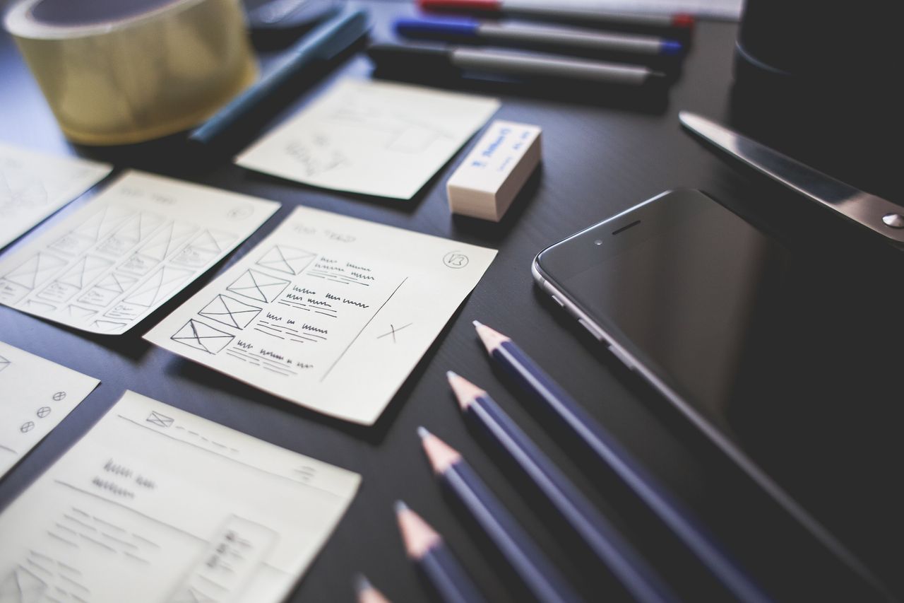 team-02 A creative workspace featuring UI design plans, pencils, a smartphone, and other office tools.